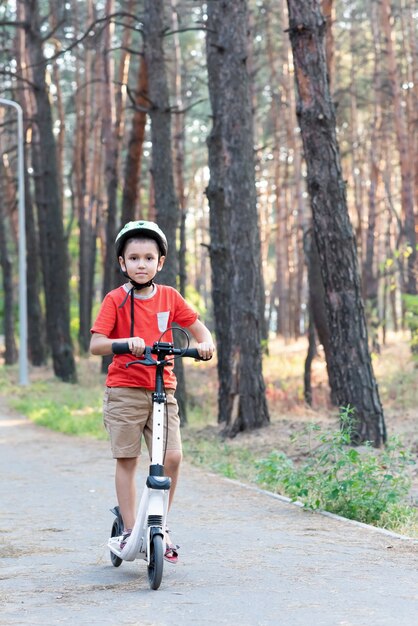 Niño montando un scooter con un casco de seguridad en el parque