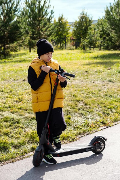 Foto niño montando un scooter eléctrico en el parque de otoño escolar usando e-scooter en un día soleado