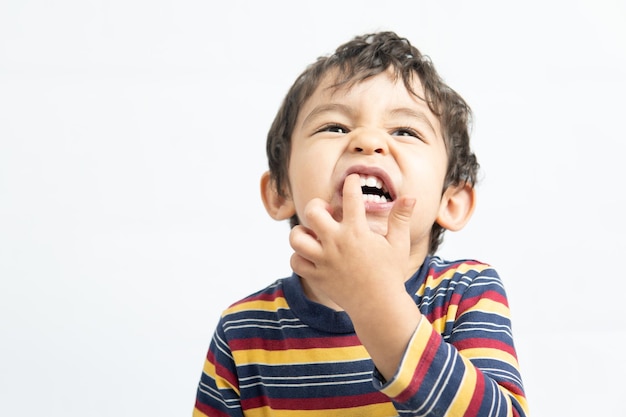 Niño mostrando los dientes con la mano sobre fondo blanco.