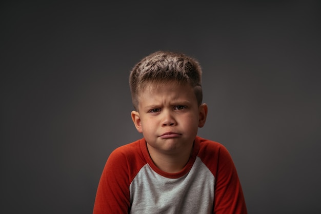 Foto niño mostrando con su rostro no me gusta a sus padres aislado sobre fondo gris