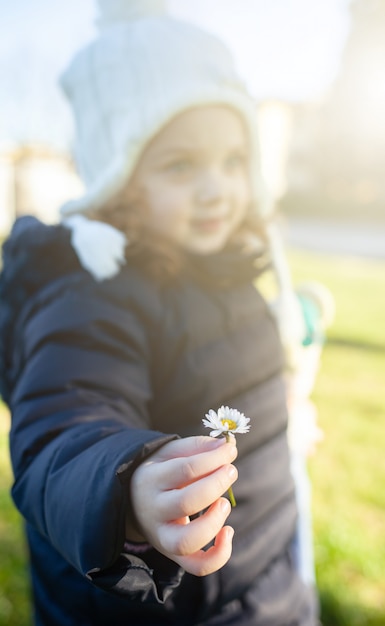 Niño de la muchacha que sostiene una flor de la margarita.