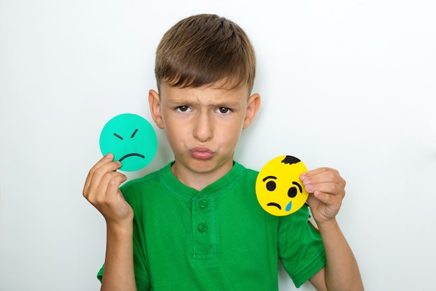 Foto el niño muestra emociones y sostiene emoticonos tristes hechos de papel.