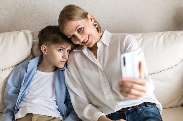 Foto niño y mujer adulta toman un selfie en el teléfono mientras están sentados en el sofá