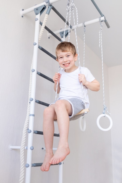 Un niño en la muralla sueca practica deportes en casa, un niño sube una escalera con una cuerda, el concepto de deporte y salud
