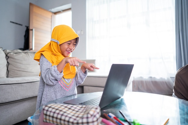 Niño musulmán joven emocionado mientras estudia en línea desde casa usando la computadora portátil