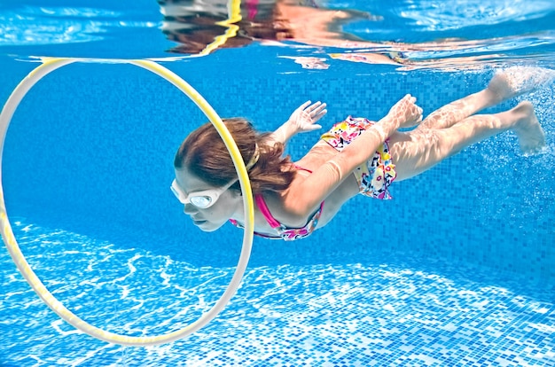 El niño nada bajo el agua en la piscina, la niña activa se zambulle y se divierte bajo el agua