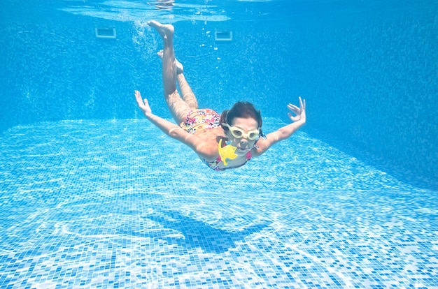 El niño nada bajo el agua en la piscina, la niña activa se zambulle y se divierte bajo el agua.