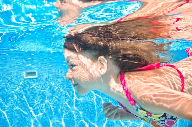 El niño nada bajo el agua en la piscina, la niña activa se zambulle y se divierte bajo el agua.