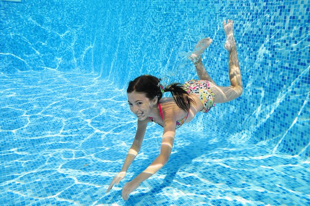 El niño nada en la piscina bajo el agua, una niña activa y feliz se sumerge y se divierte en el agua, hace ejercicio y practica deporte en vacaciones familiares