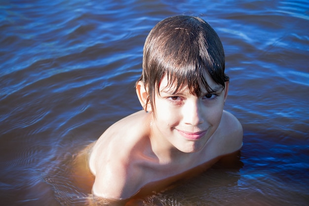 Foto niño nadando en agua azul de río, mar o lago.