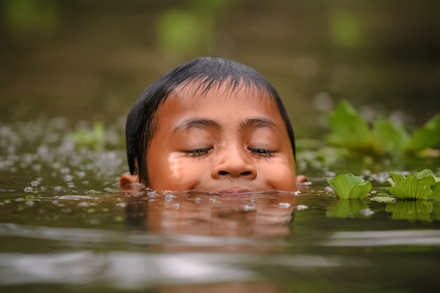 Niño nadando en el cannal cerca del mercado flotante de Damnoen Saduak