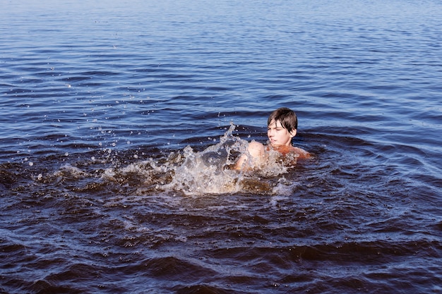 Niño nadando y chapoteando en el agua azul ondulada del río, mar o lago.