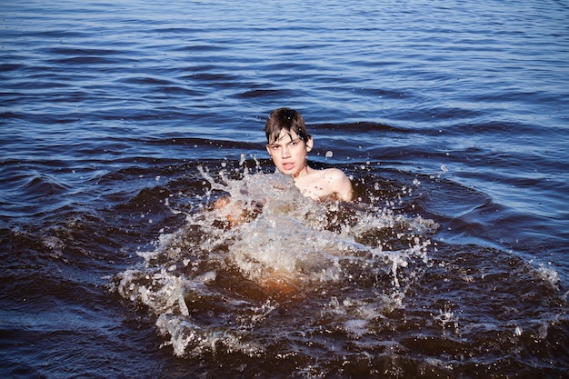 Niño nadando y chapoteando en el agua azul del río, mar o lago.
