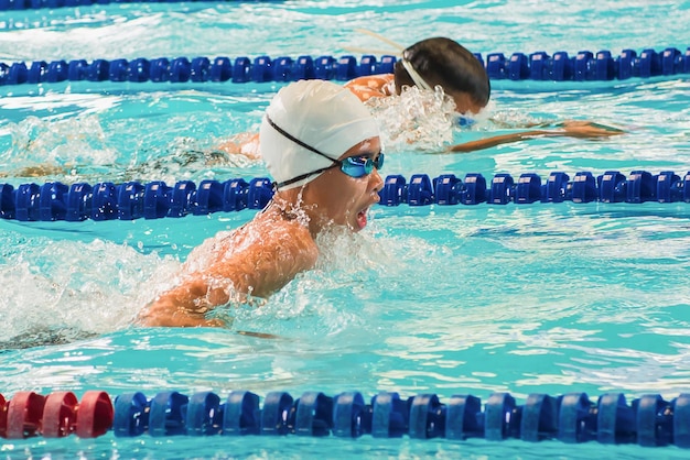 Niño nadando Mariposa en una carrera Centrarse en la cara y las gotas de agua un poco de desenfoque de movimiento Nadador profesional carrera de natación piscina cubierta