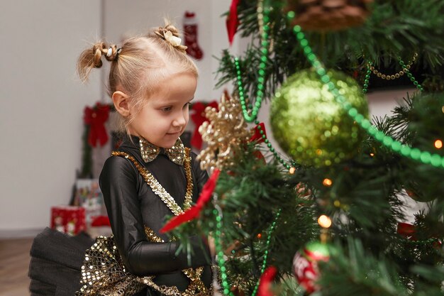 Niño de Navidad con un traje festivo decora un árbol de Navidad