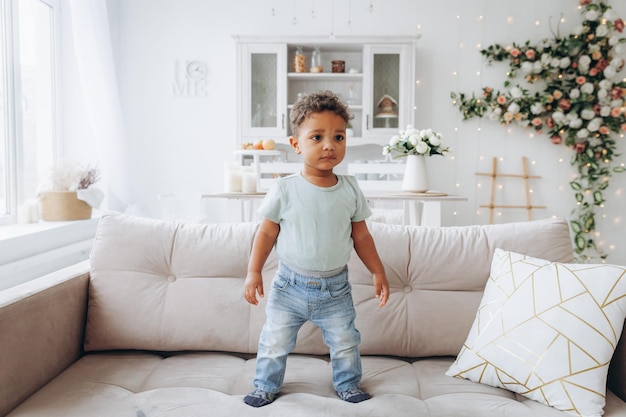 Un niño negro afroamericano feliz está parado en un sofá en la sala de estar