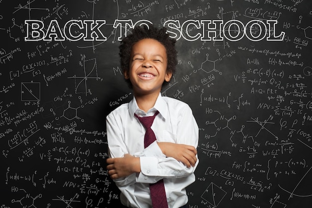 Niño negro gracioso en el fondo de la pizarra Concepto de regreso a la escuela
