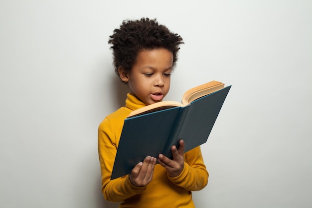 Niño negro inteligente leyendo un libro sobre un fondo blanco