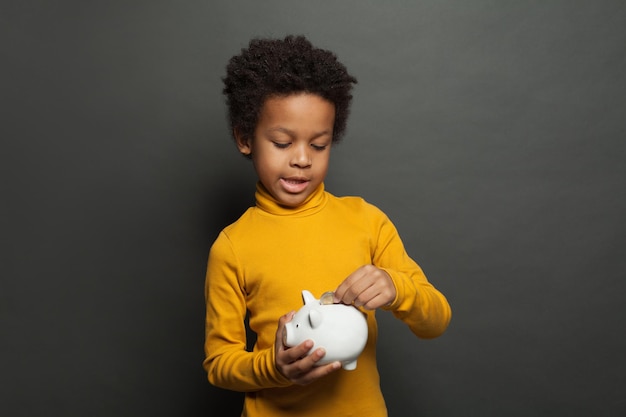 Niño negro lindo poniendo una moneda de euro en la alcancía