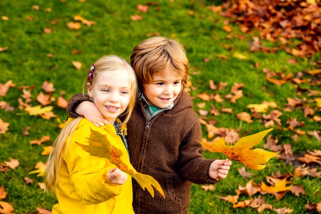 Niño y niña abrazándose en el parque otoño. Follaje colorido, hojas de arce.