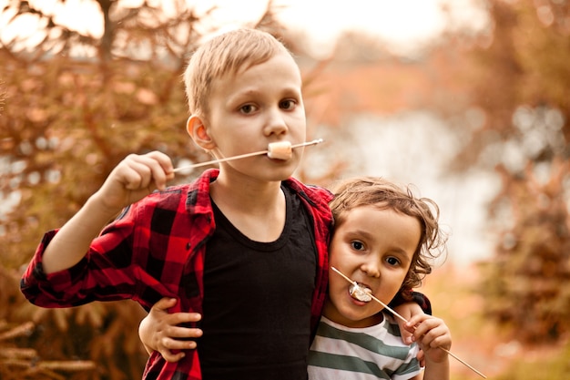 Niño y niña adolescente comiendo malvaviscos tostados al aire libre en un campamento. Viaje, caminata, vacaciones, concepto de camping.