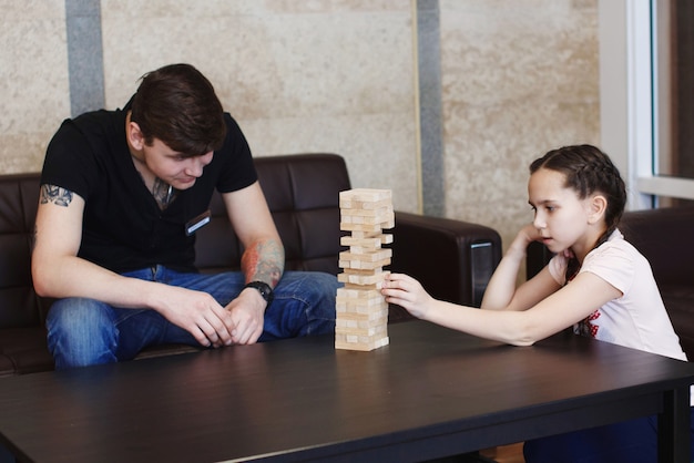 Niño y niña adolescente construyen una torre de bloques de madera del juego jenga en la mesa sentado en el sofá