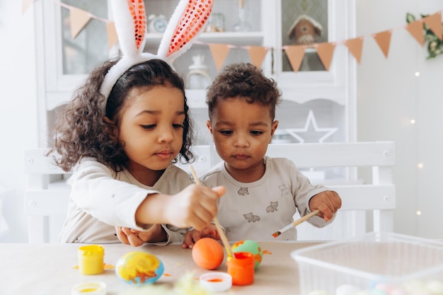 Un niño y una niña afroamericanos pintan huevos de Pascua en casa, los niños negros se están preparando para la Pascua