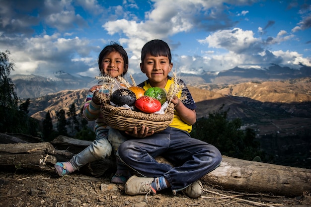 Niño y niña andina con panes de colores en el paisaje de la sierra peruana