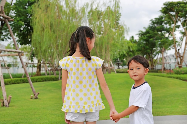 Niño y niña asiáticos cogidos de la mano mientras juegan juntos en el jardín