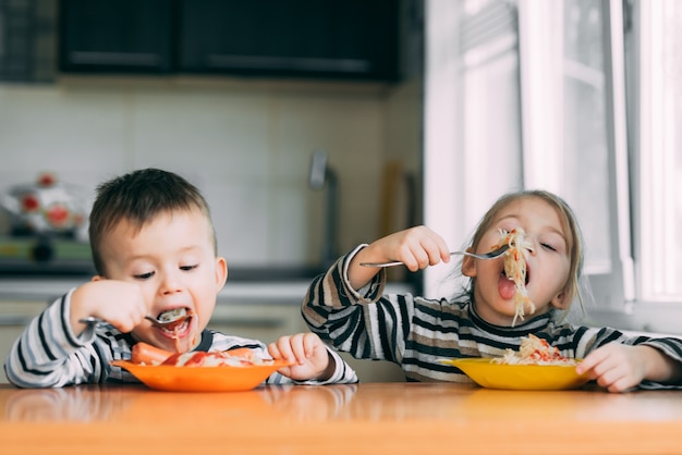 Niño y niña en la cocina comiendo pasta