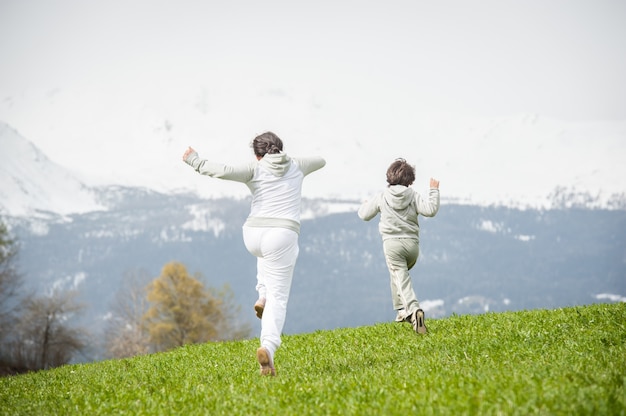 Niño y niña corriendo y saltando en el campo de primavera en los Alpes