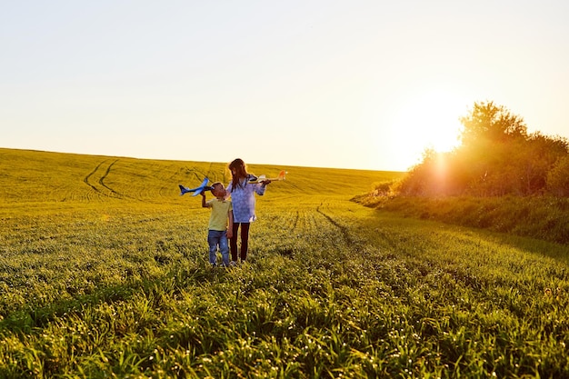 Niño y niña corriendo sosteniendo dos aviones amarillos y azules de juguete en el campo durante la puesta de sol de verano Los niños sueñan con volar y la aviación