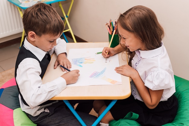 Niño y niña dibujan con lápices en la mesa