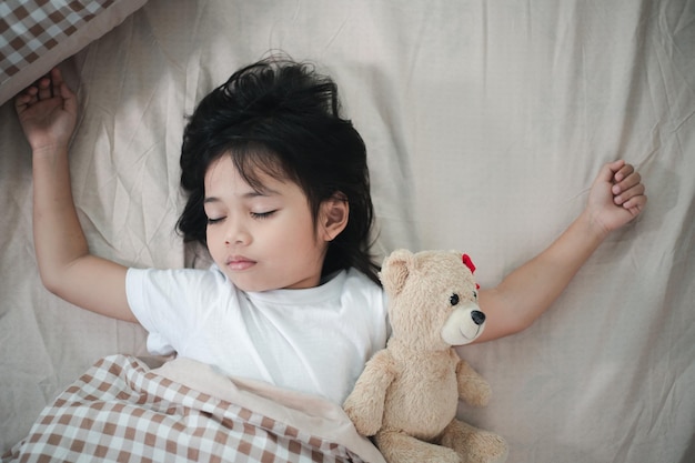 Niño niña duerme en la cama con un osito de peluche de juguete