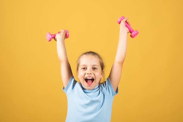 Niño niña está haciendo ejercicios con pesas sobre fondo de estudio amarillo Deporte retrato niños