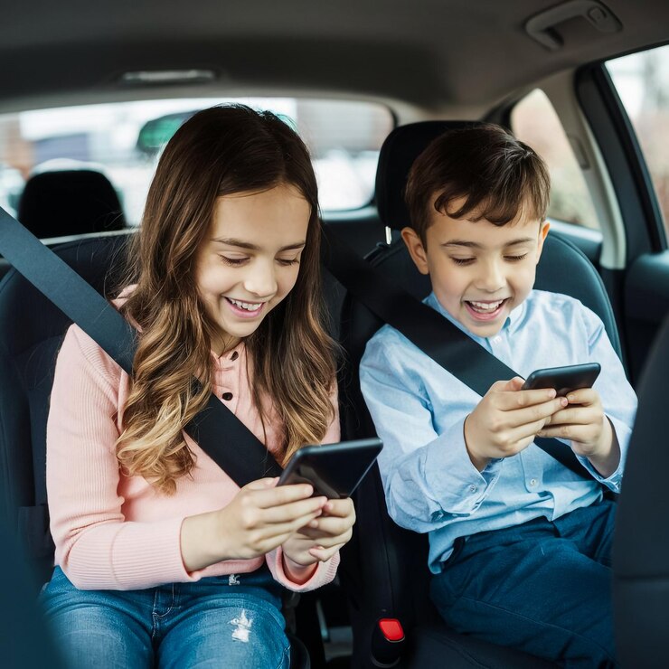 un niño y una niña están sentados en un coche y el niño está usando un teléfono celular