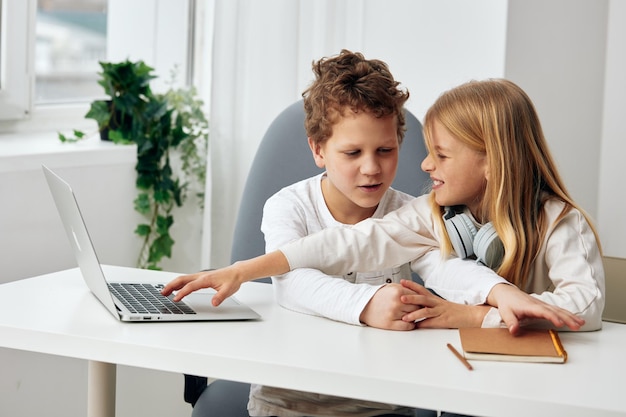 Niño y niña estudiando en línea con computadoras portátiles en casa hermanos felices involucrados en el aprendizaje electrónico sentados en un
