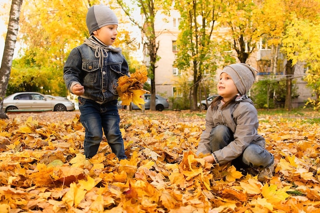 El niño y la niña felices juegan en el follaje de otoño