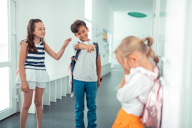 Niño y niña groseros riéndose de la niña rubia