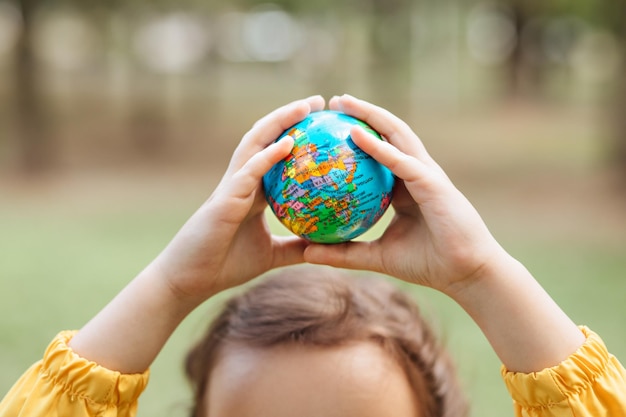 Niño niña en un impermeable amarillo sosteniendo el globo en las manos al aire libre en un parque o bosque Concepto del Día Mundial de la Tierra Energía verde Recursos renovables y sostenibles Proteger y salvar el planeta