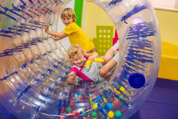 Un niño y una niña lindos jugando en Zorb, un anillo cilíndrico de plástico rodante con un agujero en el interior del medio