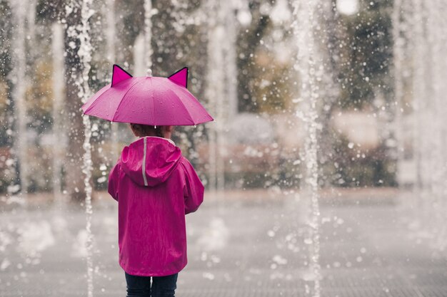 Niño, niña, llevando, impermeable, tenencia, paraguas