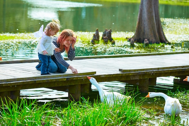 Niño niña y madre jugando con patos en el lago