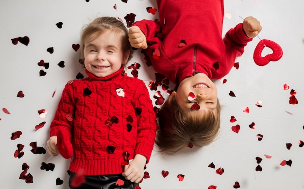 niño y niña mienten y sostienen corazones rojos sobre fondo blanco con confeti