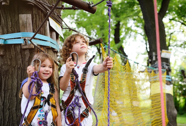 Un niño y una niña en un parque de aventuras participan en la escalada en roca o pasan obstáculos en el camino de la cuerda.