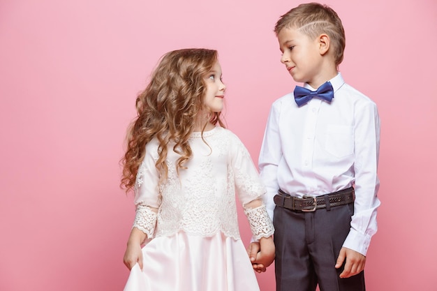 Niño y niña de pie y posando en estudio sobre fondo rosa