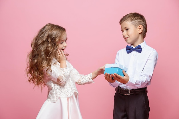 Niño y niña de pie y posando con regalo en estudio sobre fondo rosa