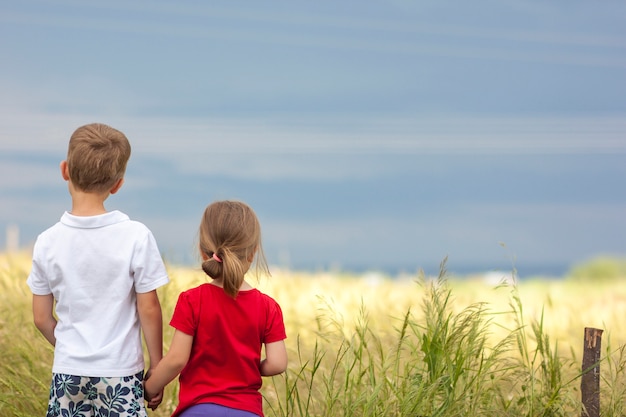 Foto niño y niña de pie tomados de la mano mirando el horizonte