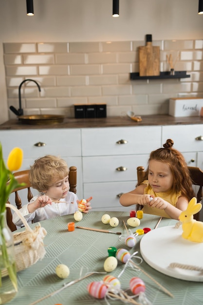 Niño y niña pintan huevos de Pascua en la cocina