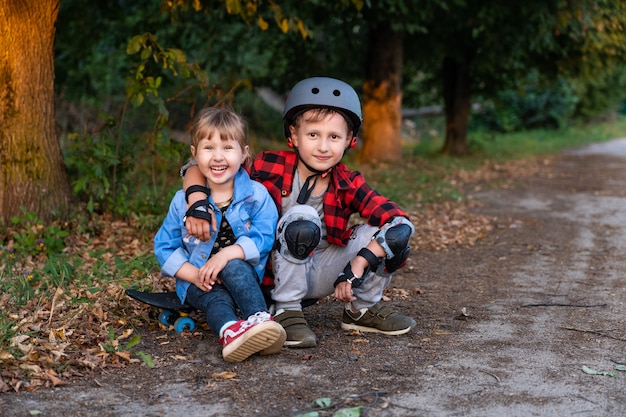 Niño con una niña sentada cerca de la carretera con una patineta